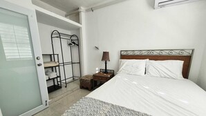 Una habitación de hotel con cama, mesita de noche, lámpara, armario y perchero.