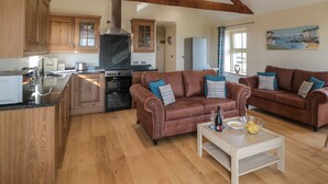 A spacious living area with two leather sofas, a coffee table, and a kitchen with wooden cabinets and a built-in oven. - Smithy Cottage (Alnwick)