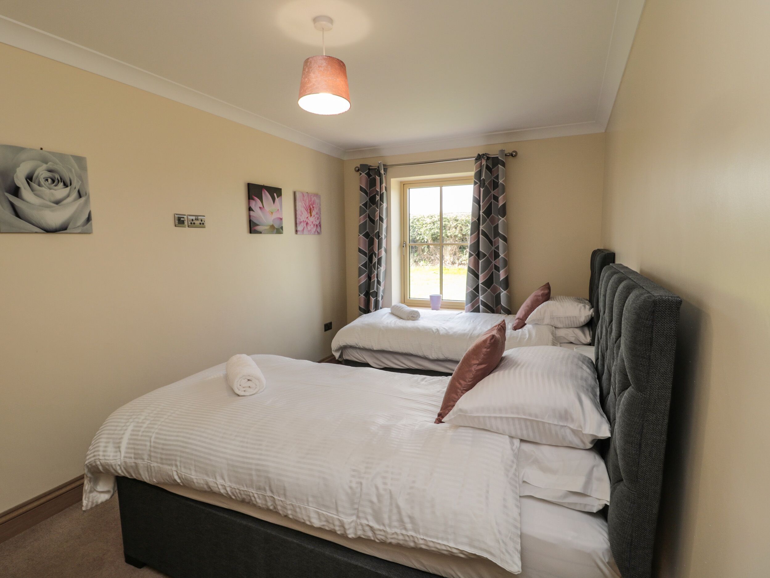 A bedroom with two beds, a window with curtains, and a hanging light fixture.