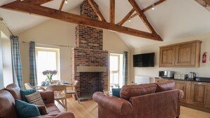 A spacious living area with a fireplace, wooden beams, a dining table with chairs, and a kitchen area with cabinets and appliances. - Smithy Cottage (Alnwick)
