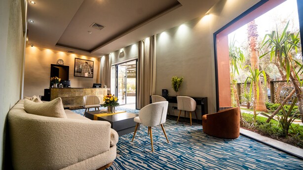 A modern hotel room with a sofa, chairs, a desk, and a view of a garden. - Avenue Echouhada (Marrakech)