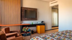 A modern hotel room with a large bed, a TV mounted on the wall, a desk with a computer, and a seating area with a chair and a small table. - Avenue Echouhada (Marrakech)
