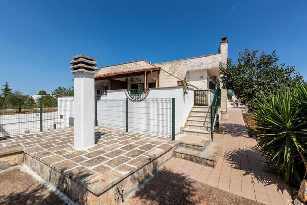 A residential property with a gated entrance, a staircase leading to a covered porch, and a paved pathway.