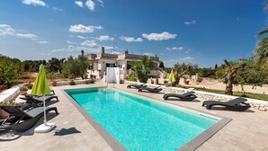 A swimming pool with lounge chairs and umbrellas, surrounded by a landscaped garden and a building in the background. - 3634 Villa Dolce - App1 by Barbarhouse (Ostuni)