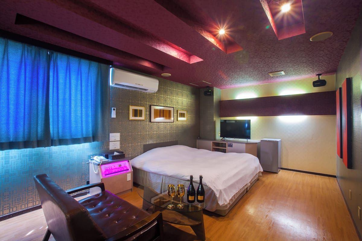 A hotel room with a bed, a desk with a computer, a chair, a TV, and a minibar.