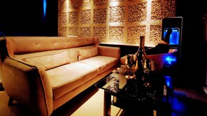 A dimly lit room with a beige sofa, a coffee table with a bottle and glasses, and a TV on a stand. - HOTEL FOURSEASON - Adults Only - (Takaoka)