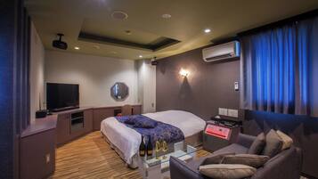 Una camera d'hotel moderna con un letto grande, una TV a schermo piatto, una scrivania con un computer e un'area salotto con divano e poltrone.