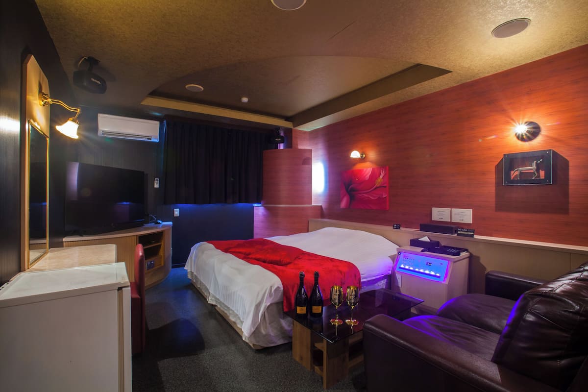 A hotel room with a bed, a desk, a TV, a minibar, and a leather couch.