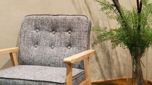 A grey upholstered chair with wooden armrests and a tufted backrest, positioned next to a glass vase with white pebbles and a green plant. - HOTEL FOURSEASON - Adults Only - (Takaoka)