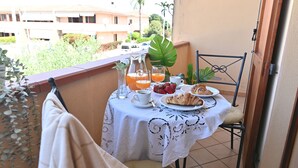 Un balcón con una mesa preparada para el desayuno, que incluye una jarra de jugo de naranja, una taza de café, un plato de cruasanes y un bol de fresas.