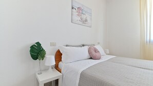 Un dormitorio ordenado con cama, mesita de noche, lámpara y una planta verde grande.