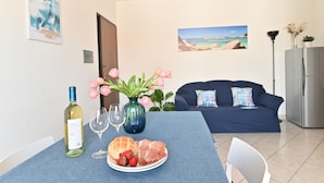 Comedor con una mesa dispuesta para dos personas, que incluye una botella de vino blanco, dos copas, un plato con pan y fresas, y un jarrón con flores rosadas.