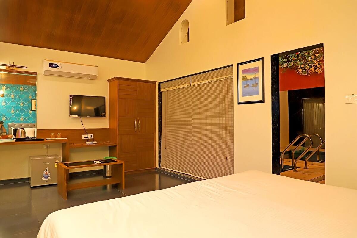 A hotel room with a bed, a desk with a computer, a wardrobe, and a sliding door leading to a balcony.
