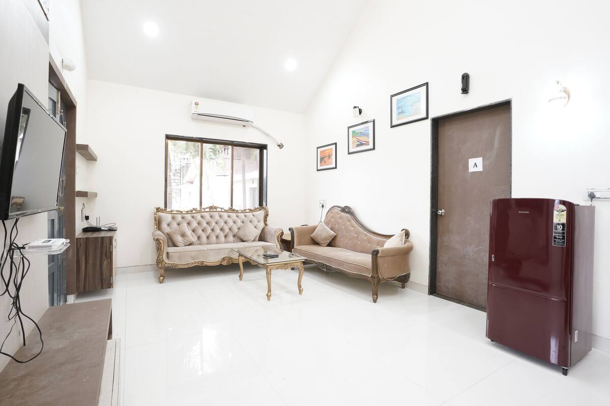 A living room with a sofa, a coffee table, a television, and a refrigerator.