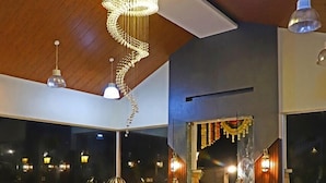 A spacious lobby with a marble floor, a wooden ceiling, and a large chandelier. There are several hanging pendant lights and a red sofa. - Siddhant Hill Resort (Murud)
