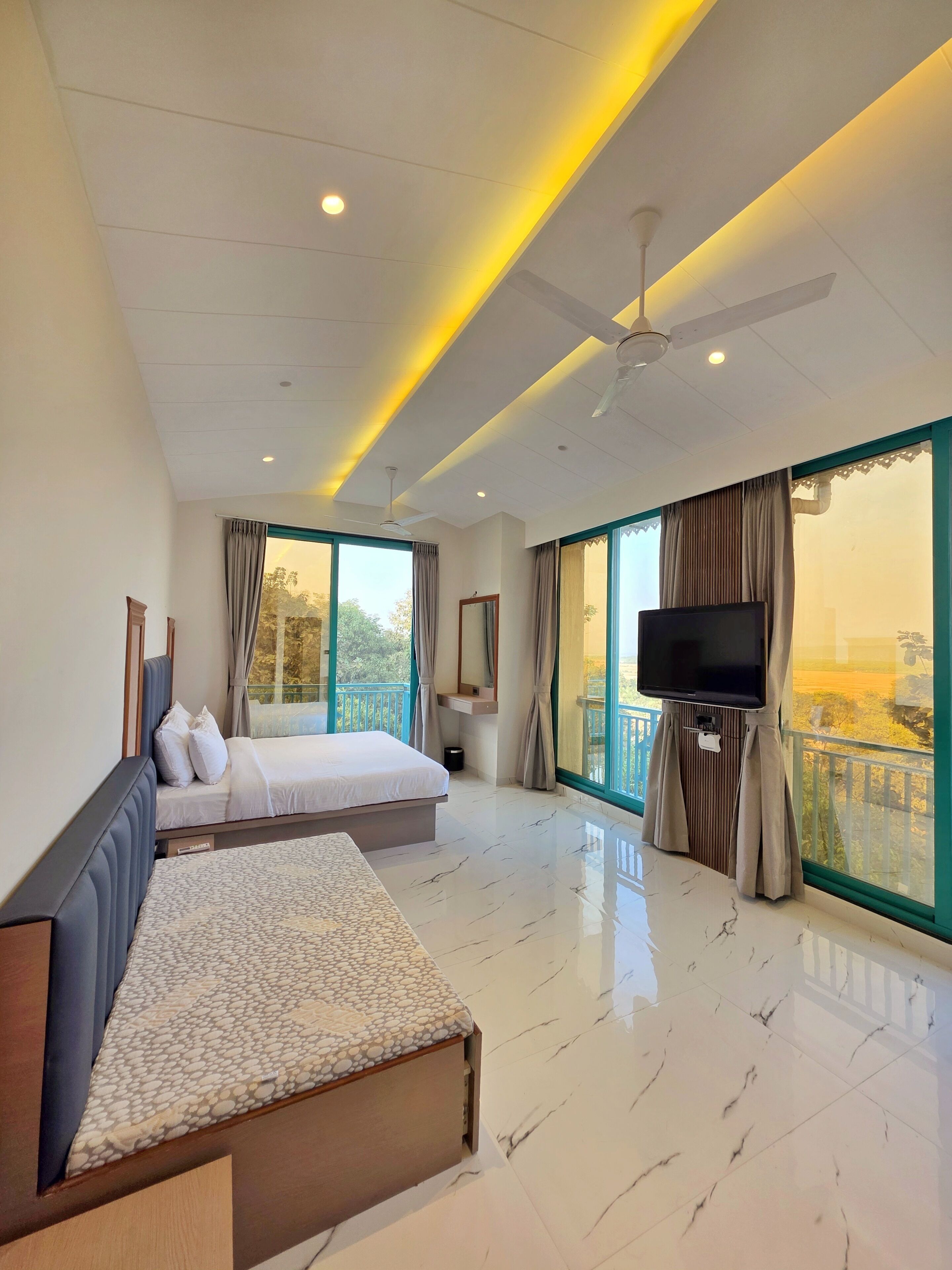 A hotel room with a bed, a sofa, a TV, and large windows with curtains.