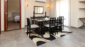 Een eetgedeelte met een glazen tafel en stoelen, een spiegel, wandlampen en een kamerbreed tapijt.