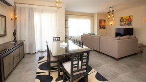 Een moderne woonkamer met een glazen eettafel, een beige bank en een flatscreen televisie.