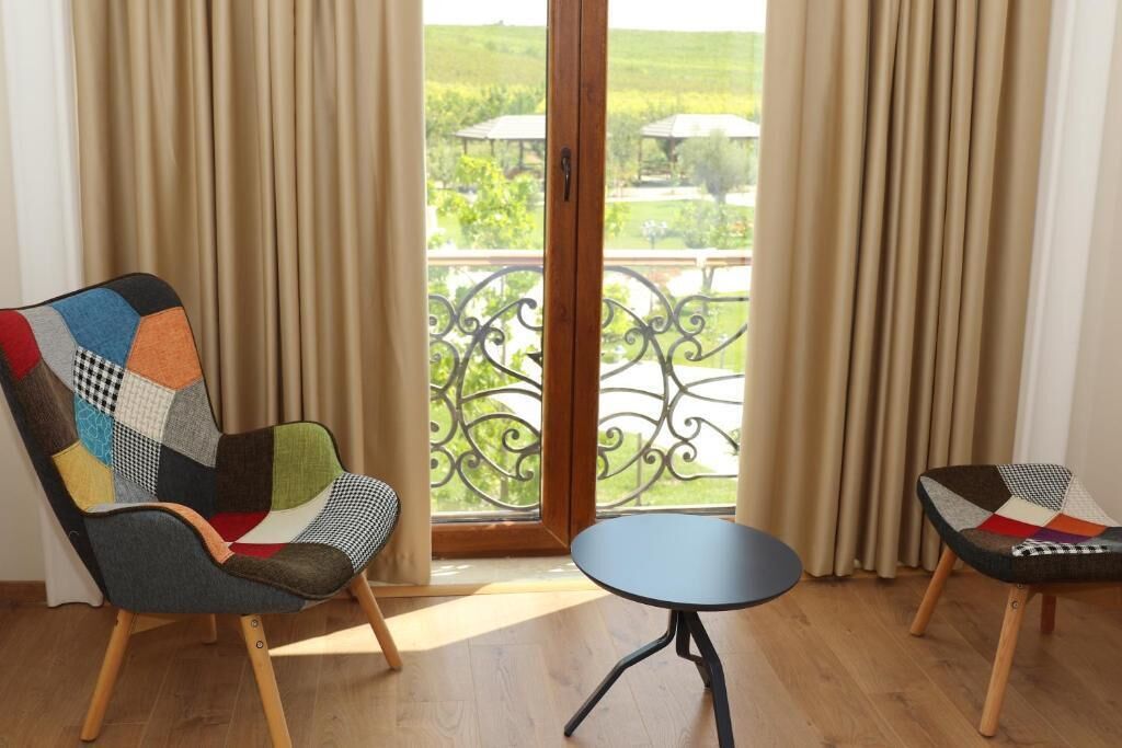 A room with a large window, two chairs with patchwork upholstery, and a small round table.