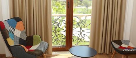 A room with a large window, two chairs with patchwork upholstery, and a small round table.
