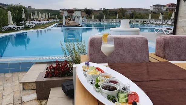 A poolside dining area with a table set for a meal, a pool, and lounge chairs in the background. - Vinea Resort & SPA (Rrashbull)