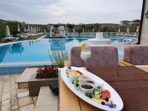 A poolside dining area with a table set for a meal, a pool, and lounge chairs in the background. - Vinea Resort & SPA (Rrashbull)
