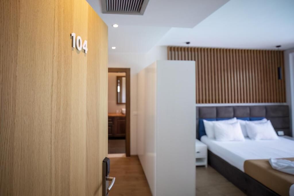 A hotel room with a wooden wall, a bed with white bedding, and a visible number '104' on the wall.