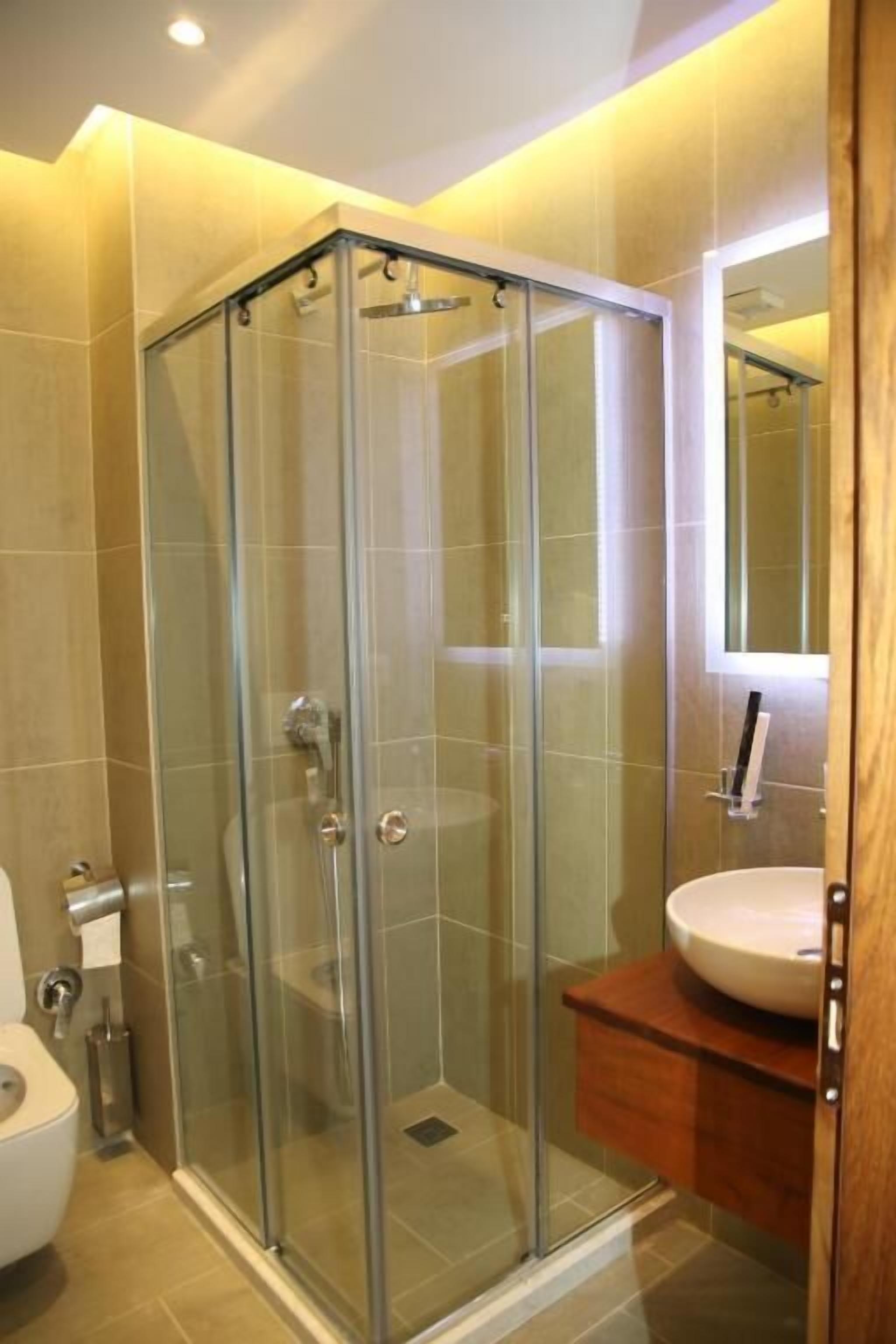 A modern bathroom with a glass-enclosed shower, a white sink, and a wooden vanity.