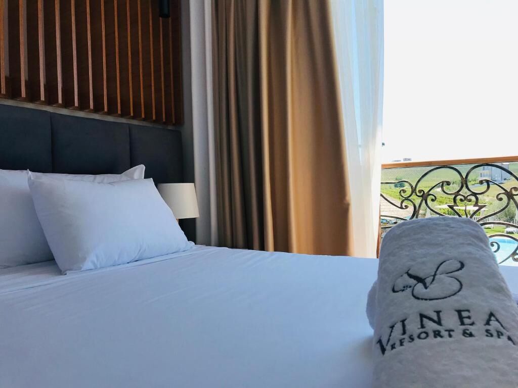 A hotel room with a bed, white bedding, a headboard, and a view of a pool and greenery outside.