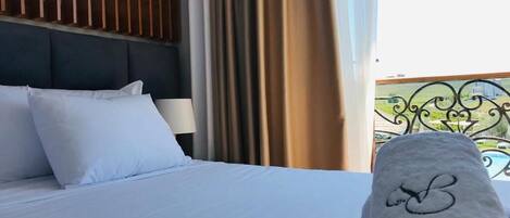 A hotel room with a bed, white bedding, a headboard, and a view of a pool and greenery outside.