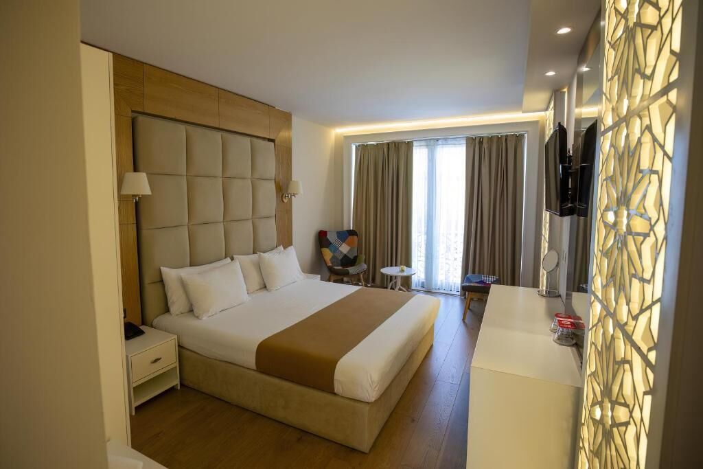 Una habitación de hotel con una cama grande, mesitas de noche, un escritorio, una silla, un televisor y un panel decorativo en la pared.