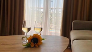 A table with two wine glasses and a sunflower, a sofa, and a view through sheer curtains. - Vinea Resort & SPA (Rrashbull)