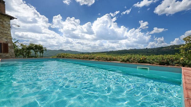 A clear blue pool with a stone building on one side and a view of green hills under a partly cloudy sky. - Fienile al Corno, Radda in Chianti, Siena and Chianti (Radda in Chianti)