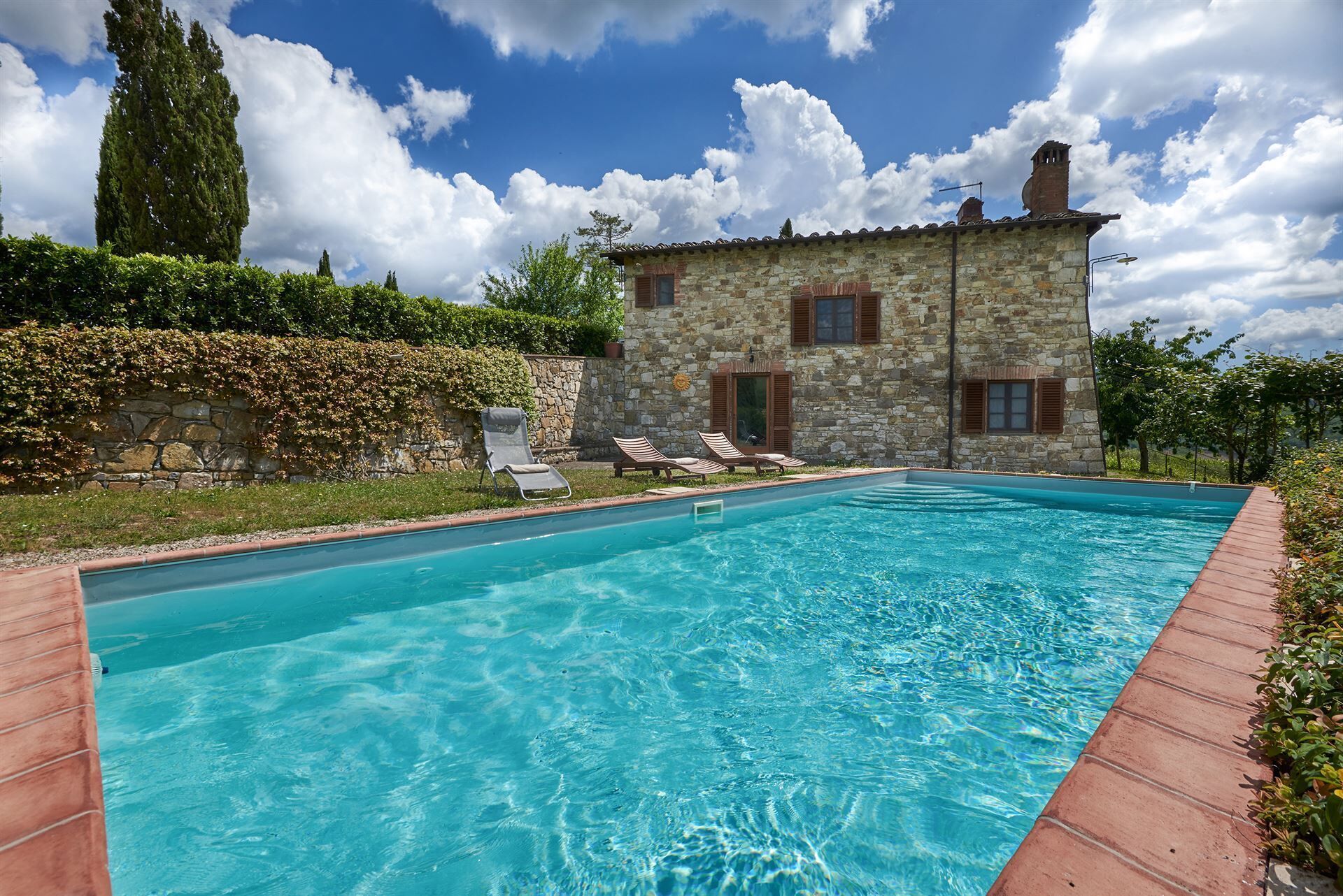 A stone building with a swimming pool, surrounded by greenery and a clear sky.