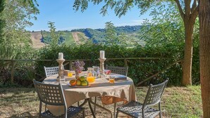 An outdoor dining table with a view of rolling hills, surrounded by chairs and a tablecloth. - Il Pascolo, San Gimignano, Siena and Chianti (San Gimignano)
