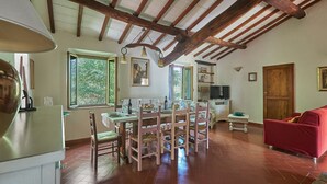 A dining area with a wooden table and chairs, a television, and a red sofa in a rustic room with exposed wooden beams and large windows. - Il Pascolo, San Gimignano, Siena and Chianti (San Gimignano)