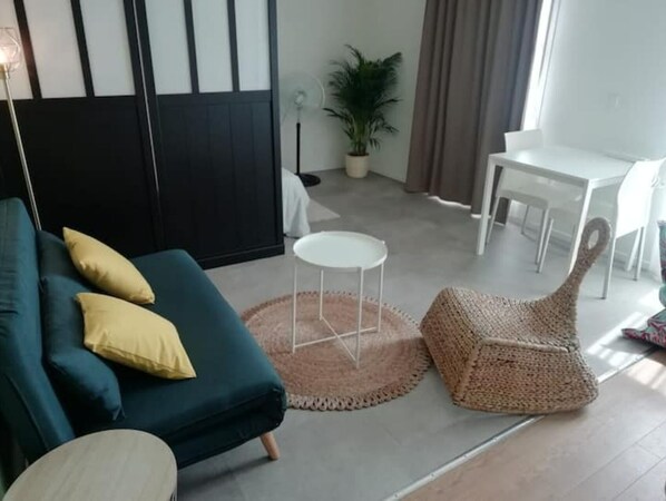 Un salon moderne avec un canapé de couleur turquoise, une table basse ronde, un pouf en fibres tressées et une table à manger avec des chaises.