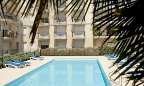 Une piscine entourée de chaises longues, elle-même bordée d’un immeuble à plusieurs étages doté de balcons.
