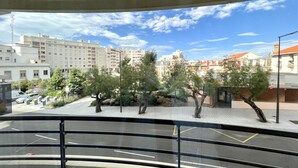 Blick vom Balkon auf einen Parkplatz mit Bäumen und Gebäuden im Hintergrund.