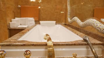 A bathroom with a large bathtub, marble countertops, and gold fixtures.
