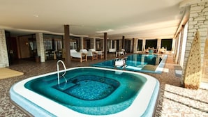 Una piscina interior con un jacuzzi, sillones de descanso y una pared de piedra.
