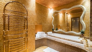 Un baño lujoso con un toallero de tono dorado, un espejo grande con marco decorativo y una zona de lavabo con azulejos.
