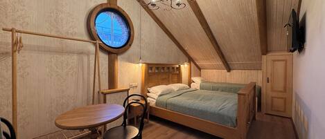 Un dormitorio acogedor en el ático con techo de madera, un ventanal redondo, una cama, una mesa y sillas.