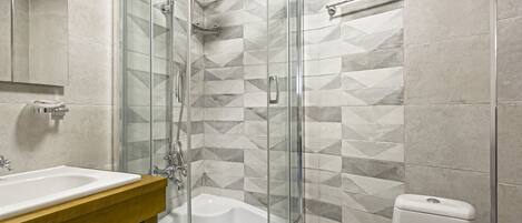 A modern bathroom with a glass-enclosed shower, a white bathtub, and a toilet.