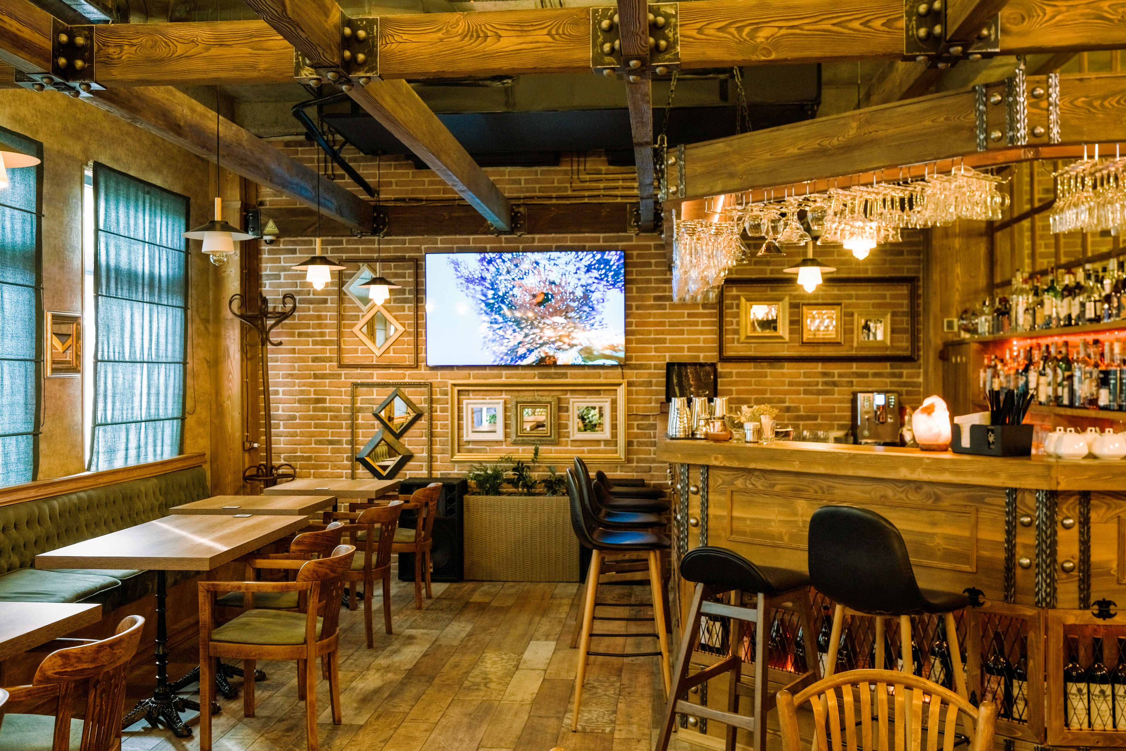 A cozy bar area with wooden tables and chairs, a brick wall, and a television screen.