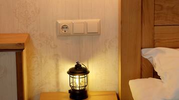 Una mesita de noche de madera con un farol, un enchufe de pared y una cama con ropa blanca.