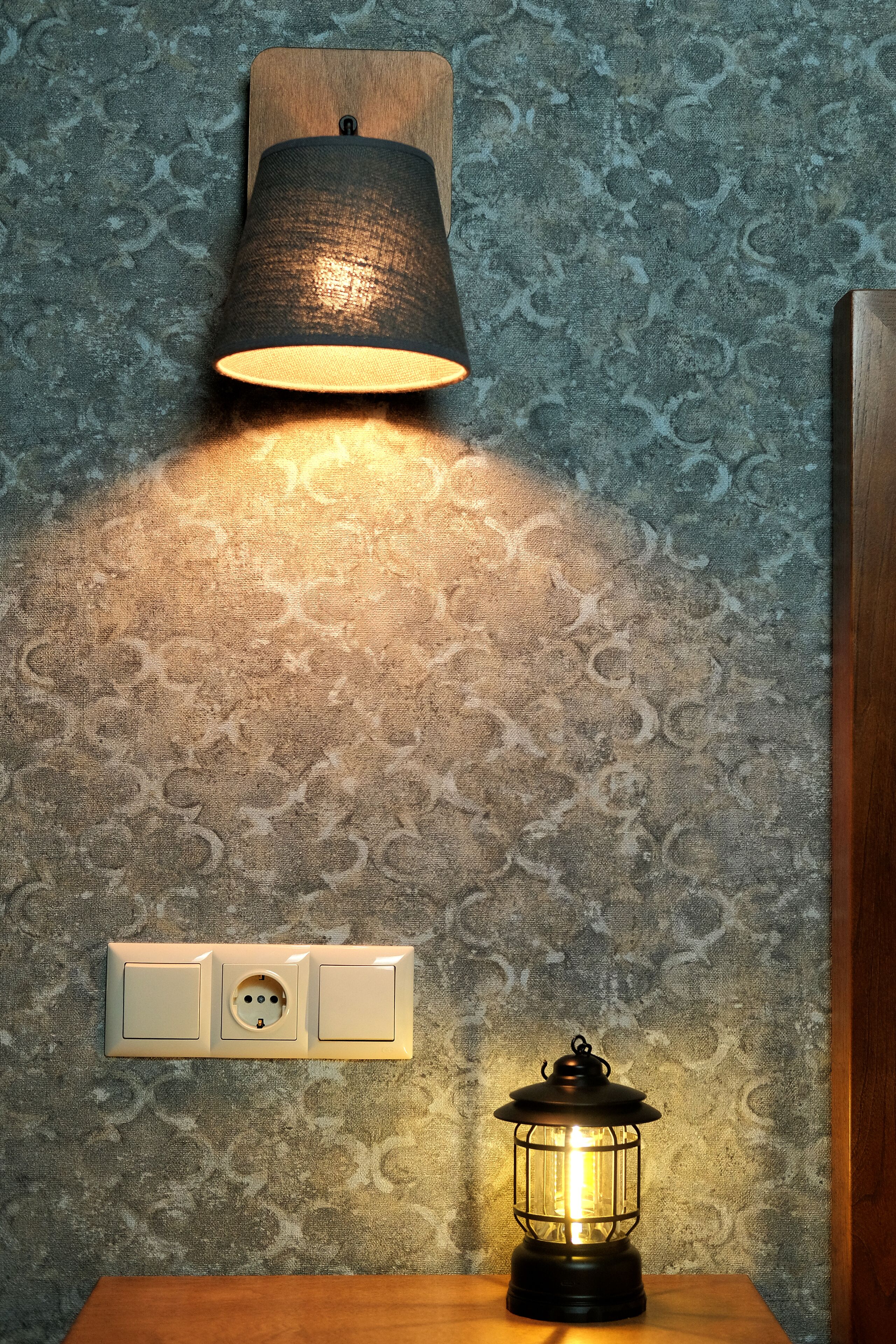 Una lámpara de pared con pantalla cilíndrica, un enchufe y una lámpara de mesa con estructura de vidrio.