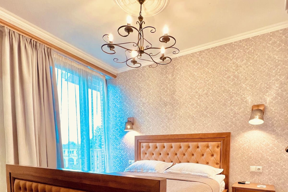 A bedroom with a wooden bed, a chandelier, a nightstand, and a window with curtains.