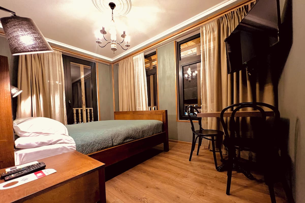 A hotel room with a bed, a desk with a chair, a TV, and a chandelier.