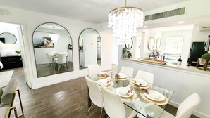 A modern dining area with a glass table, white chairs, and a chandelier.